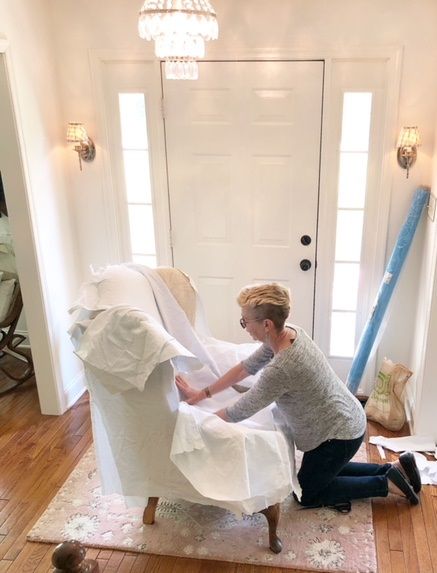 Jeanne pinfitting a camelback sofa with a white cotton denim fabric in a client's living room. 